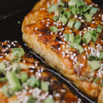 Two maple-glazed salmon fillets in cast iron skillet